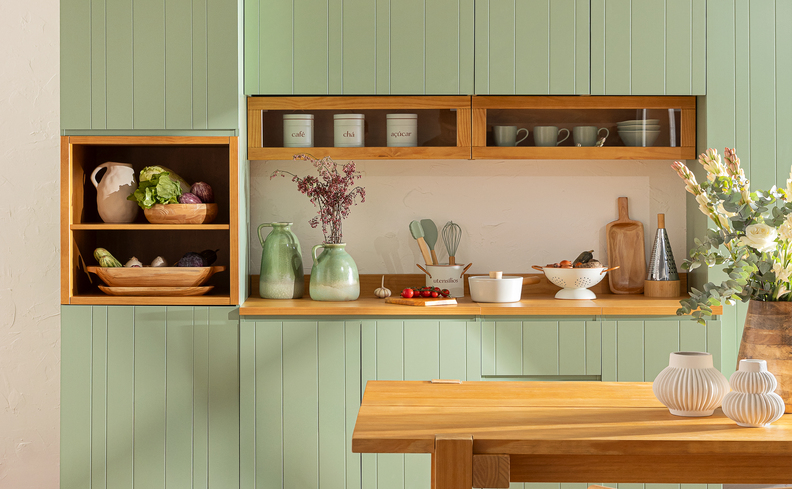 utensílios de cozinha em um ambiente completo com armários verde e em tons de madeira claro, além de itens como pratos, canecas, potes e diversos itens decorativos.