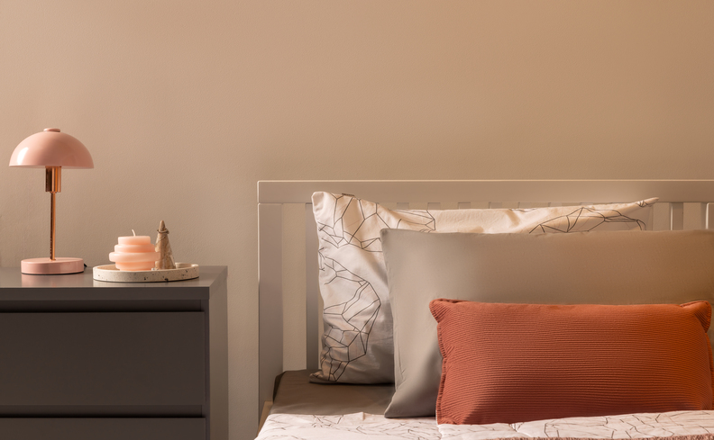 decoração de quarto de menina adolescente com mesa de cabeceira, abajur, cama de solteiro e diversos travesseiros.