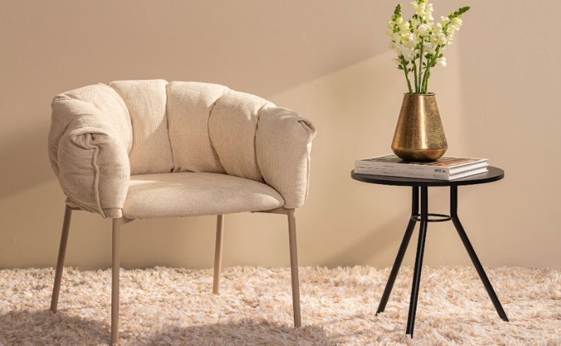 poltrona de presente de casa nova com design assinado, além de um tapete, mesa de apoio e um vaso com uma flor.