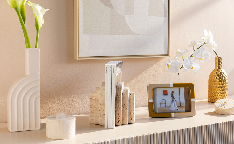 vasos decorativos para rack de sala em tons neutros, além de porta-retrato, aparador de livros, velas aromáticas e outros itens de decoração.