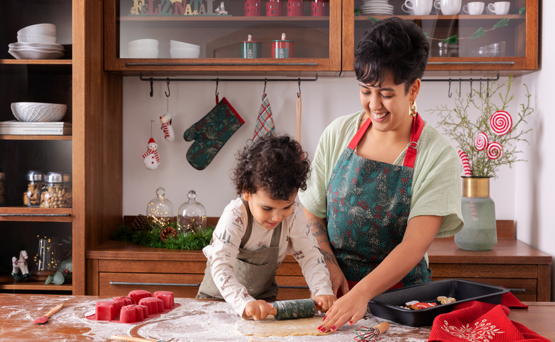 brincadeiras para fazer no natal com mãe e filho fazendo biscoitos natalinos na cozinha decorada com itens de natal.