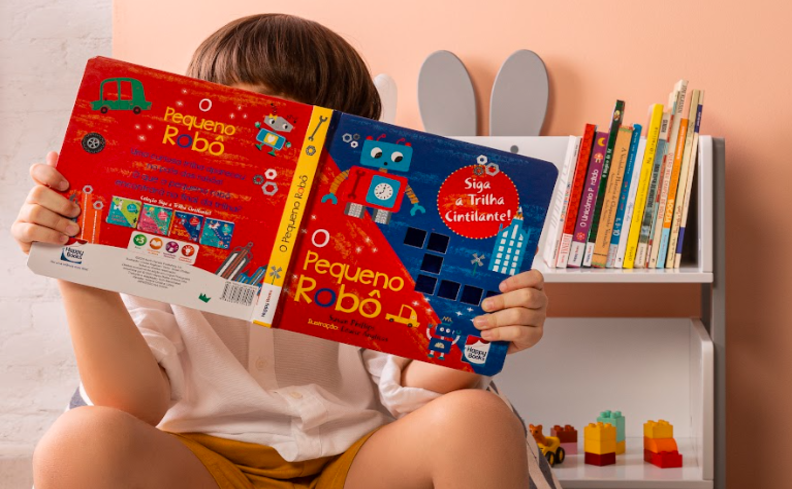 menino sentado em um cantinho da leitura no quarto lendo um livro de histórias para crianças