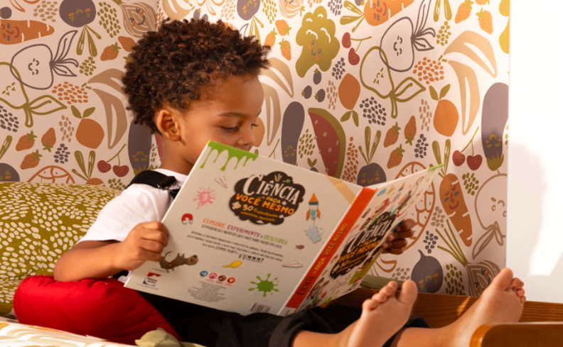 livros para criança ler e estimular a imaginação, com um menino sentado em um cantinho da leitura infantil no quarto para estimular esse hábito.