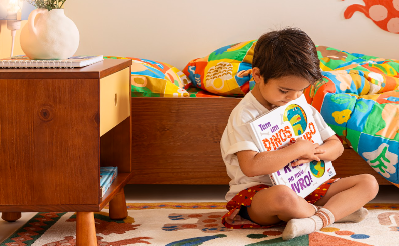 livros para crianças de 10 anos e outras idades, com um menino sentado no quarto abraçando seu livro preferido.