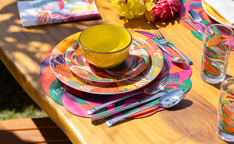 decoração de carnaval simples em casa com jogo americano, pratos raso, fundo e tigela, além de copos com estampas vibrantes e coloridas.