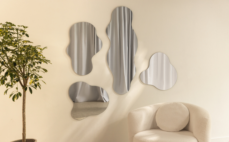 espelhos decorativos para sala de jantar em diversos tamanhos em um formato orgânico, além de uma poltrona e um vaso com planta.