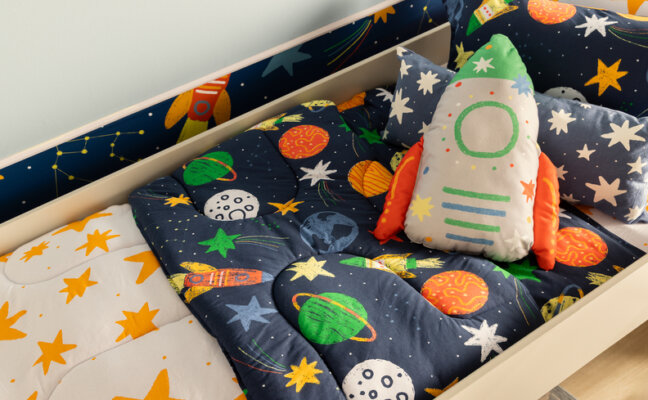 decoração de quarto astronauta e via láctea com roupa de cama, almofada de foguete em tons de azul, branco e laranja.