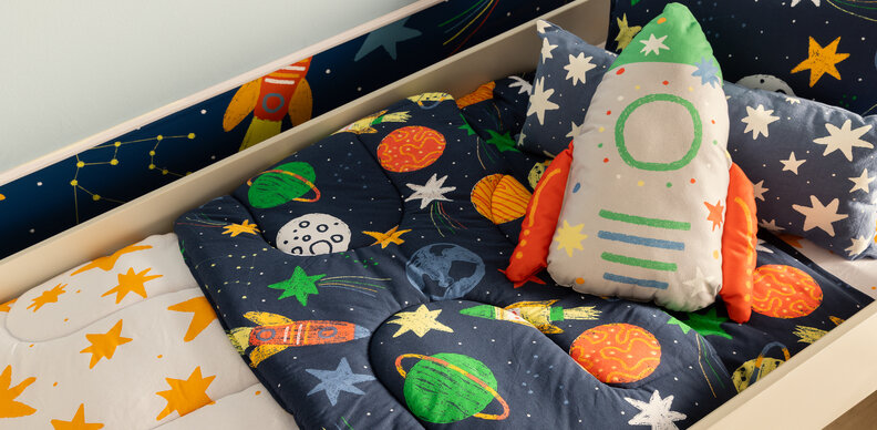 decoração de quarto astronauta e via láctea com roupa de cama, almofada de foguete em tons de azul, branco e laranja.