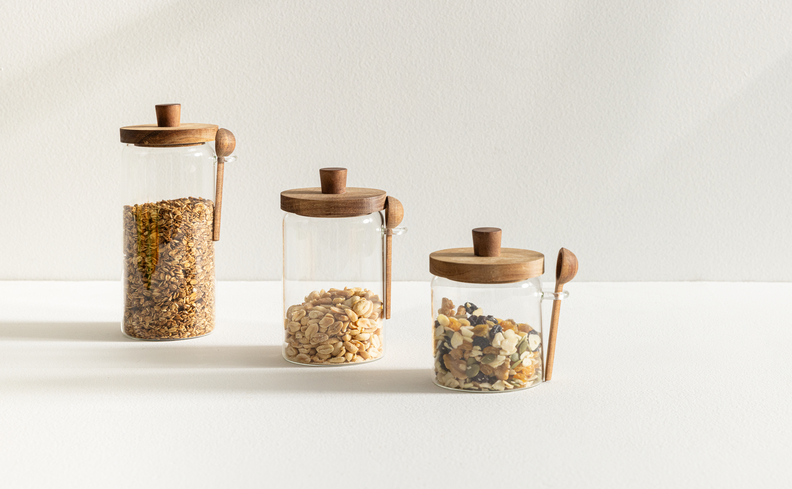 potes organizadores de alimentos em diversos tamanhos e tampa de bambu, além de uma colher ao lado para facilitar na hora de pegar os alimentos.