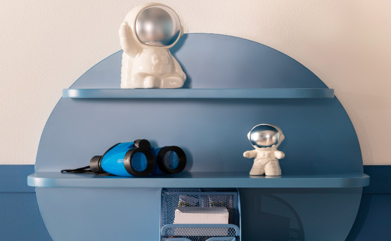 quarto infantil astronauta com prateleiras azul e adornos de astronauta em branco, além de um binóculo e itens de papelaria.