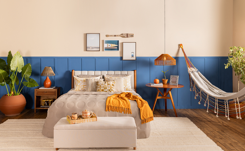 quarto tons de azul na parede e tons de amarelo na roupa de cama para usar cores vibrantes na decoração com uma harmonia no ambiente, além de rede, pendente, cama, quadros decorativos e vasos com plantas.