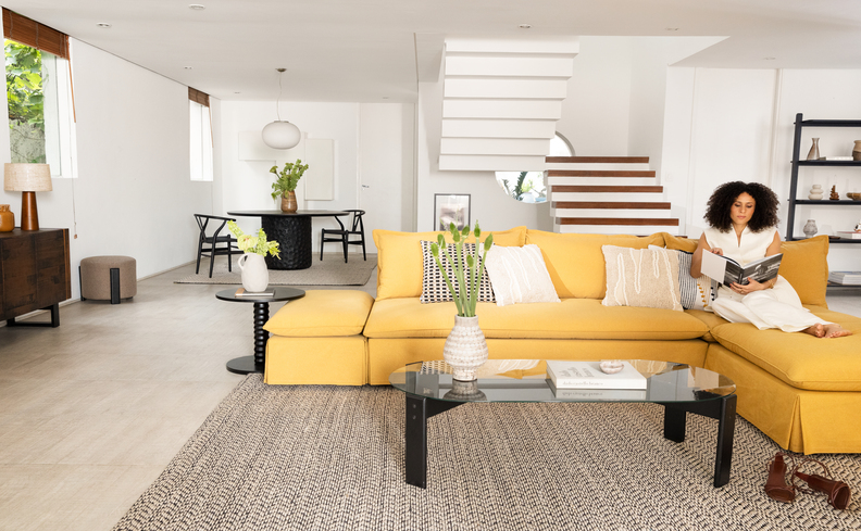 sala de estar com sofá amarelo com chaise e para criar uma harmonia, os demais itens presentes no ambiente são de cores neutras para equilibrar a decoração.