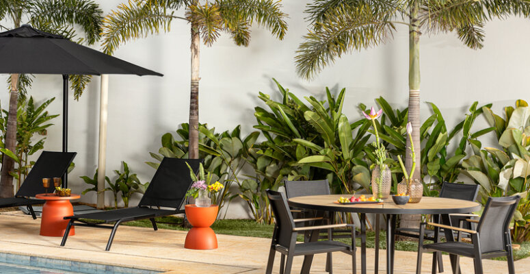 plantas pet friendly para ter em casa e oferecer segurança para os animais, em uma varanda com diversas plantas, vasos, mesa com quatro cadeiras, ombrelones e espreguiçadeiras.