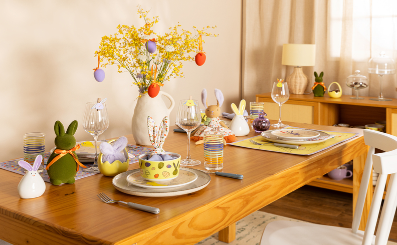 café da manhã de Páscoa simples com mesa posta completa com vaso com ovos decorativos, pratos, copos, adornos em formato de coelho, talheres e guardanapo.