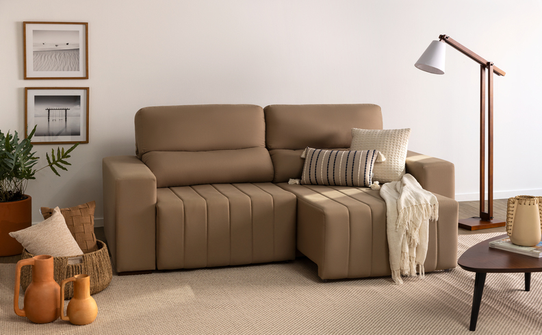 sofá pequeno retrátil na cor cinza, além de manta para sofá, almofadas, luminária de chão, mesa de apoio, quadros decorativos e vasos com plantas.