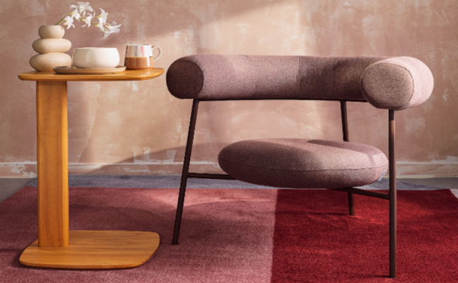 cantinho da leitura na sala de estar com poltrona, tapete e uma mesa de apoio com vaso com planta, caneca de chá e um vaso decorativo para aproveitar o Dia Mundial do Livro com conforto e beleza.