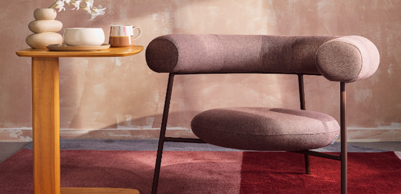 cantinho da leitura na sala de estar com poltrona, tapete e uma mesa de apoio com vaso com planta, caneca de chá e um vaso decorativo para aproveitar o Dia Mundial do Livro com conforto e beleza.