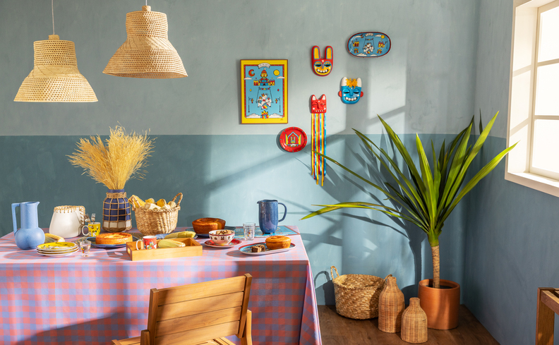 decoação de festa junina em casa com mesa com toalha xadrez, vaso com plantas, lustre pendente de palha e diversas comidas típicas dessa época.