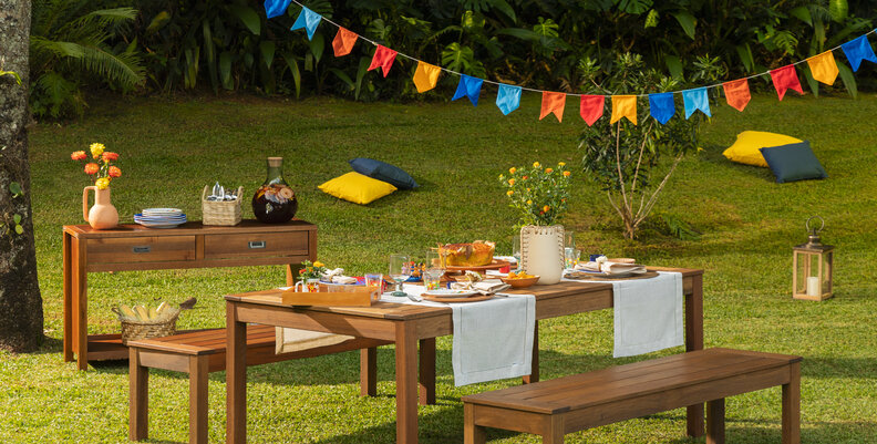 festa junina simples em casa com brincadeiras para reunir e divertir toda a família em um quintal grande com mesa retangular, bancos, decoração de festa junina, mesa posta e um aparador para auxiliar.