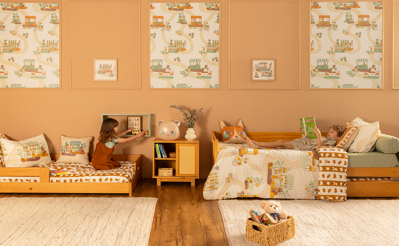 quarto infantil com um espaço para a leitura, com duas camas, diversos itens decorativos, cômoda com diversos livros e um tapete confortável para as crianças aproveitarem