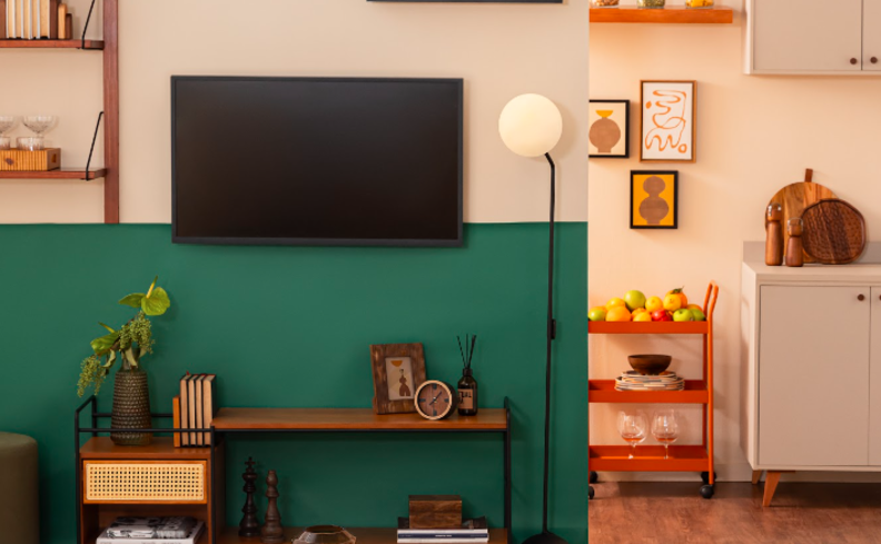 carrinho de bar na cozinha usado como fruteira, em um ambiente com a sala de estar com parede verde e diversos móveis como rack, prateleiras e armários na cozinha.