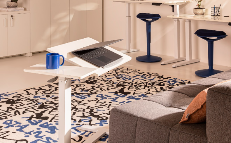 decoração home office com sofá, mesa regulável, banquetas, mesa grande, caneca, almofadas e outros itens para compor o escritório compartilhado em casa.