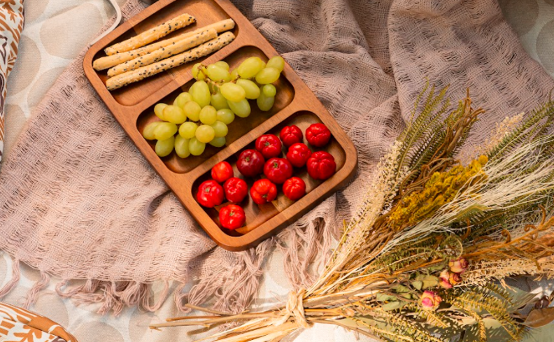 dicas para saber como fazer fondue em casa com diversas opções de acompanhamentos como tomates, uvas e palitinho de parmesão em uma tábua com divisórias em uma mesa com toalha e flores secas.