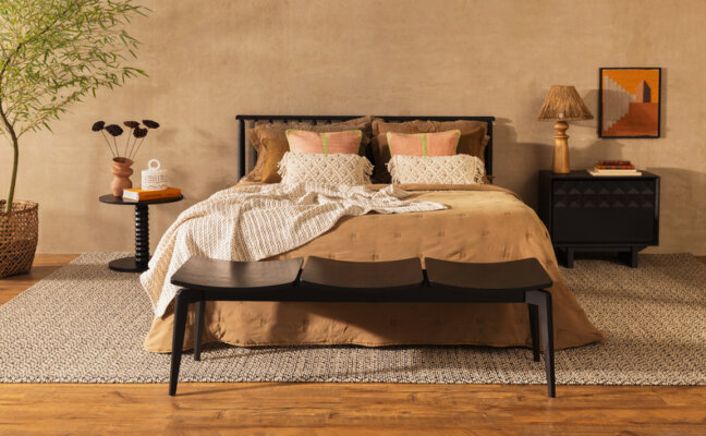 decoração boho em casa no quarto com tons neutros e terrosos com cama, peseira, roupa de cama, almofadas e travesseiros. Além de tapete, mesas de cabeceira, luminária de mesa e quadros decorativos e vasos com plantas.