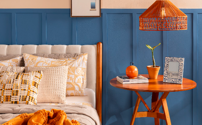 decoração boho simples no quarto com mesa de cabeceira de madeira, lustre pendente de rattan, quadros decorativos e uma cama com roupa de cama em tons terrosos.