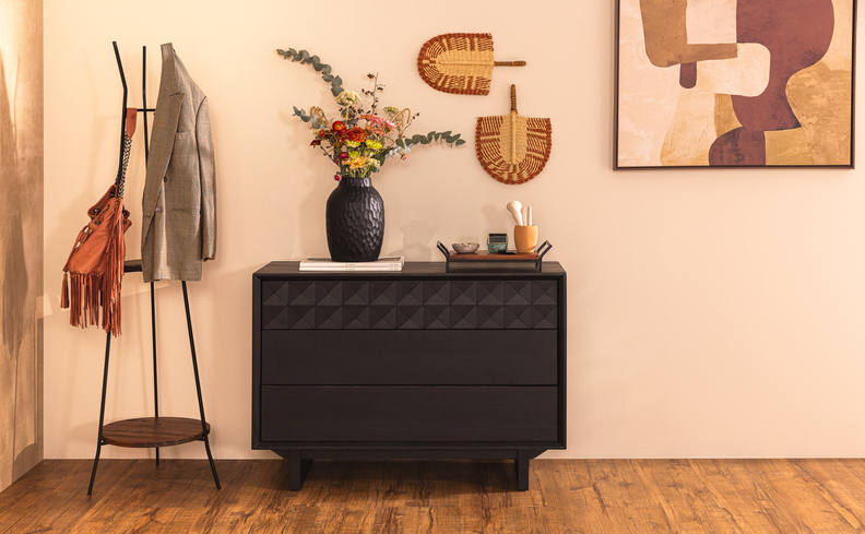 decoração boho na entrada da casa com buffet aparador, cabideiro, quadro decorativo, adornos de palha na parede e vaso com planta.