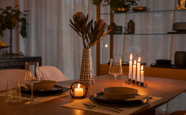 noite de vinho e fondue em casa com uma mesa posta completa, com centro de mesa com vaso com flores, velas, pratos fundos, sousplat, jogo americano, talheres e taças para criar um ambiente intimista.