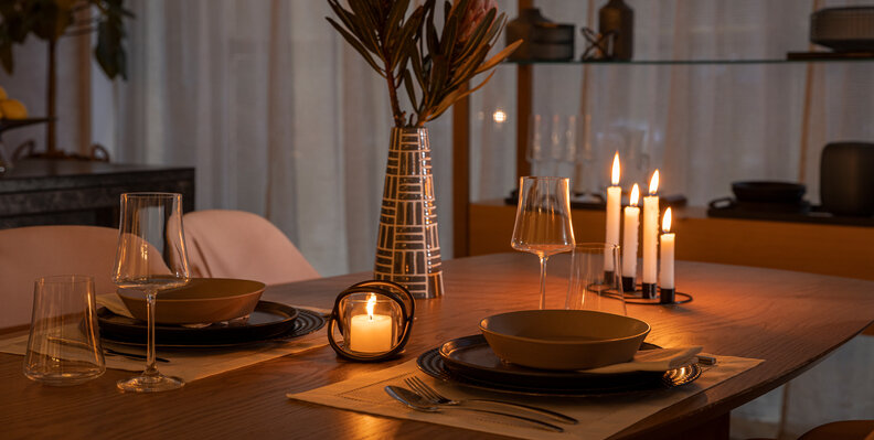 noite de vinho e fondue em casa com uma mesa posta completa, com centro de mesa com vaso com flores, velas, pratos fundos, sousplat, jogo americano, talheres e taças para criar um ambiente intimista.