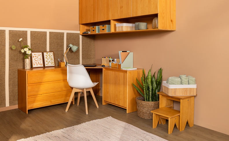 escritório em casa em um canto em L no quarto, com escrivaninha, cadeira de escritório, tapete, itens de organização, armários aéreos e vasos com plantas.