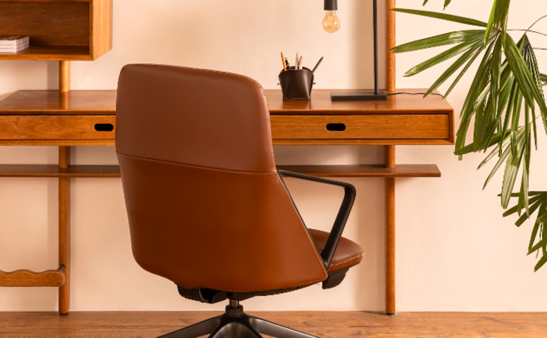 home office pequeno no quarto com cadeira de escritório marrom, escrivaninha com estante, vaso com planta, porta lápis e outros itens de escritório.