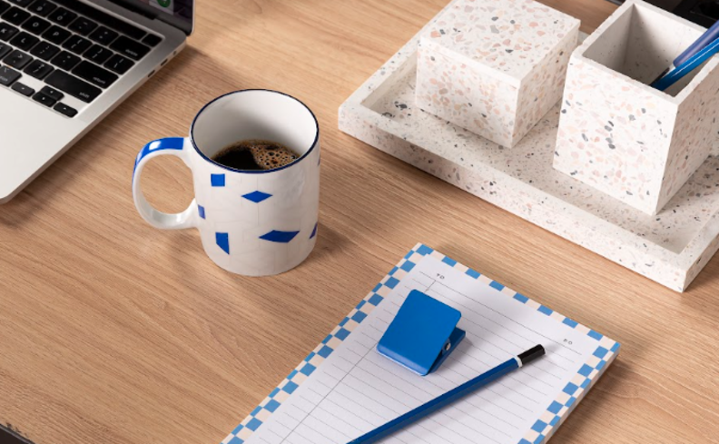 ideias para home office pequeno com bloco de anotações, lápis, organizado de porta-lápis, caneca com café em uma escrivaninha compacta.