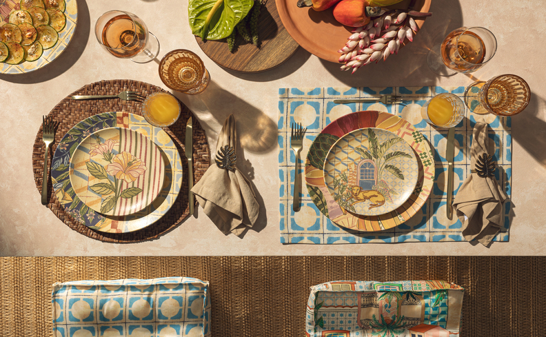 mesa posta com pratos, guardanapo de tecido, argola para guardanapo, taças e copos, além de fruteiras com banana, maça e outras frutas.