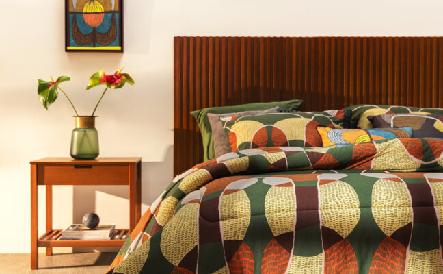 altura de cabeceira de cama em um quarto de casal com cama posta em tons de marrom, laranja e verde, além de cabeceira, mesa de cabeceira e diversos itens decorativos.