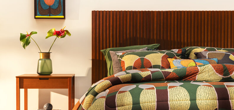 altura de cabeceira de cama em um quarto de casal com cama posta em tons de marrom, laranja e verde, além de cabeceira, mesa de cabeceira e diversos itens decorativos.