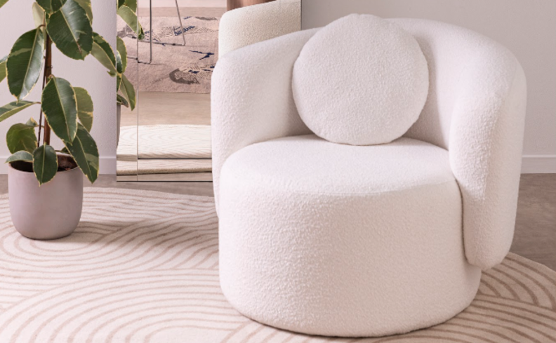 melhor poltrona para leitura em um modelo orgânico na cor branca com um encosto redondo para as costas, além de um vaso com planta ao lado e tapete branco.