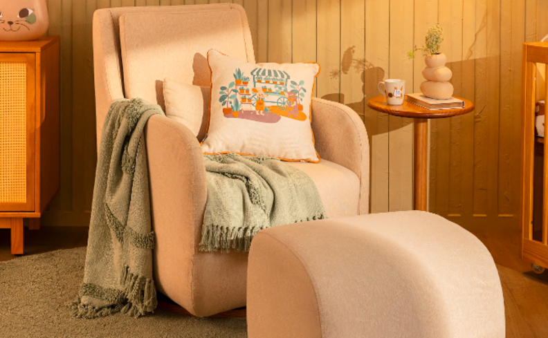 poltrona confortável para leitura em um modelo giratório na cor bege com apoio para os pés, além de manta e almofada em um quarto com mesa de apoio e cômoda.