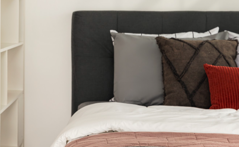 tamanho ideal cabeceira cinza em um quarto de casal com cama, colchão, roupas de cama, travesseiros e almofadas nas cores marrom, vermelho e cinza.