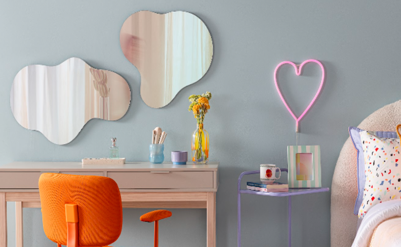 como escolher espelho orgânico grande para parede no quarto com escrivaninha penteadeira, cadeira laranja, cama e itens decorativos.